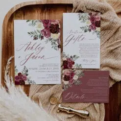 Printable burgundy wedding invitation card featuring burgundy flowers, cream blooms, and rustic greenery leaves. Elegant fall wedding design.